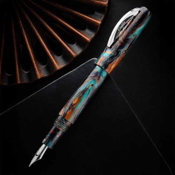 A close-up shot of a Conklin 1898 Bohemian Twilight fountain pen. The pen features a vibrant, swirling pattern of dark blue, teal, and orange resin. The pen has a silver clip and a trimless cap.