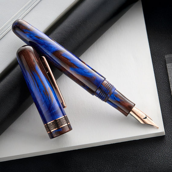 A close-up shot of a Conklin 1898 Mariana Trench fountain pen, showcasing swirls of blue and brown on the resin body, rose gold trim, decorative band around the base of the cap, and distinctive 