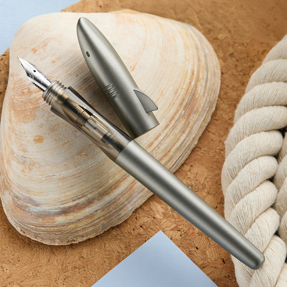 Silver fountain pen on a textured surface with a shell and rope