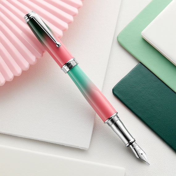Gradient pink to green fountain pen on a light surface with notebooks.
