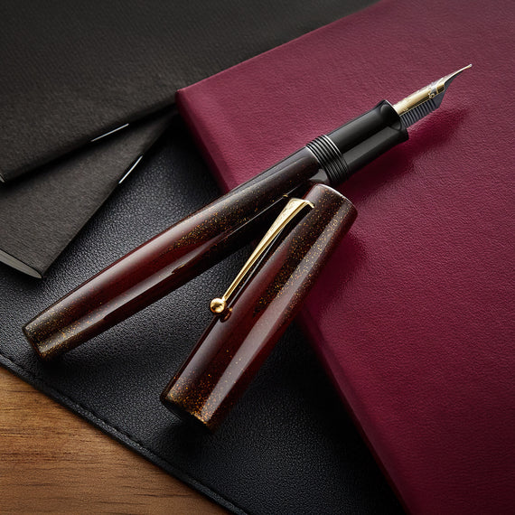 Brown fountain pen on a red leather surface with a black background