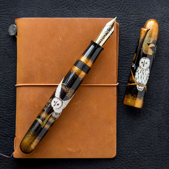 Fountain pen with owl design on a brown leather notebook against a dark background