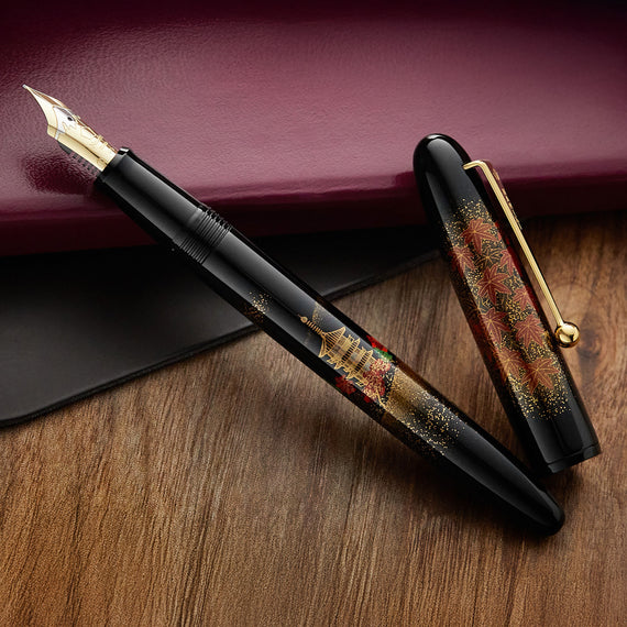 An ornate fountain pen and its cap on a wooden surface with a maroon background