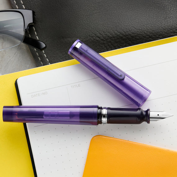Purple fountain pen on a notebook with glasses in the background