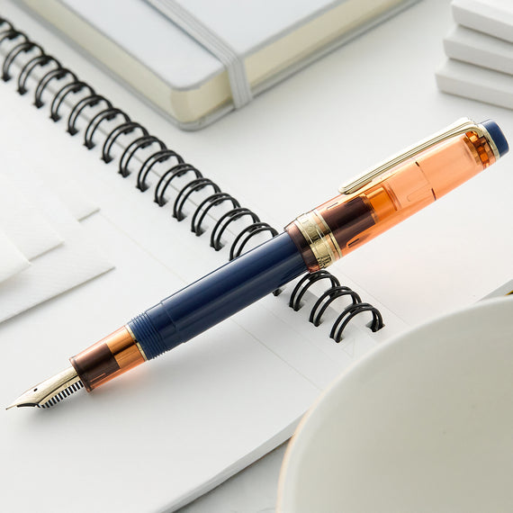 Fountain pen with blue and orange accents on a white surface with a notebook.