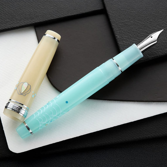 A fountain pen, in beige and turquoise, on a dark surface.