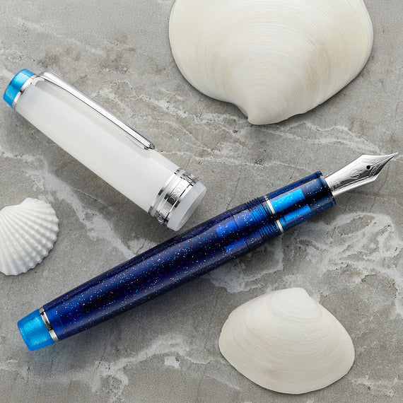Blue and silver fountain pen on a gray surface with seashells