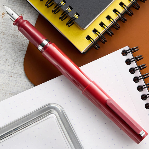 Red fountain pen on a white surface with notebooks in the background