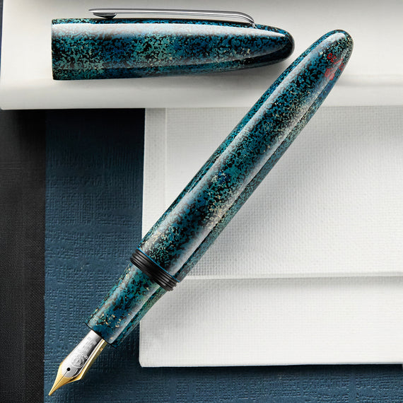 Blue speckled fountain pen on a white surface with a blue notebook.